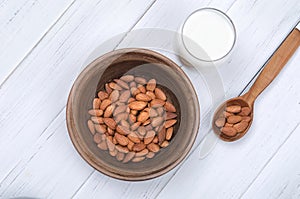 Flatlay view of almond milk in glass with seeds and wooden spoon on white table