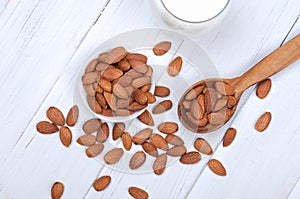 Flatlay view of almond milk in glass with seeds and wooden spoon on white wooden table