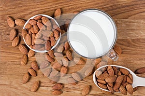 Flatlay view of almond milk in glass with seeds and wooden spoon on wooden table