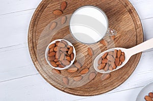 Flatlay view of almond milk in glass with seeds and wooden spoon on wooden table