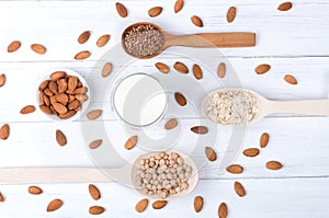 Flatlay view of almond milk in glass with seeds and wooden spoons on white wooden table