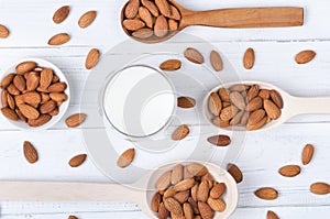 Flatlay view of almond milk in glass with seeds and wooden spoons on white wooden table plate