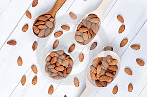 Flatlay view of almond milk in glass with seeds and wooden spoons on white wooden table plate