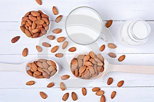 Flatlay view of almond milk in glass with seeds and wooden spoons on white wooden table plate