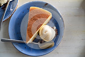 Flatlay view of cheesecake and vanilla ice cream a la mode on a blue plate with spoon