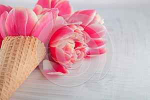 Flatlay waffle sweet ice cream cone with pink tulips blossom flowers over white wood background