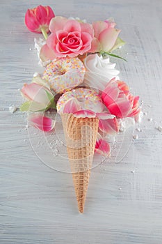 Flatlay waffle sweet ice cream cone with pink tulips and roses blossom flowers over white wood background, top view