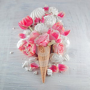 Flatlay waffle sweet ice cream cone with pink tulips and roses blossom flowers over white wood background, top view