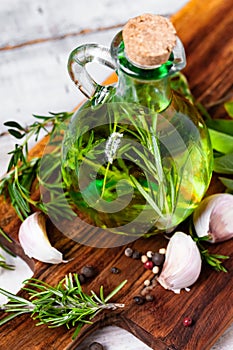 Flavored fresh naturalolive oil with herbs: rosemary, sage, thyme, garlic, pepper in glass bottle on wooden board. Wooden