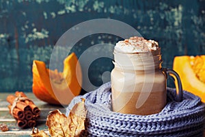 Flavored pumpkin spiced latte or coffee in cup decorated knitted scarf on teal vintage background. Autumn, fall, winter hot drink.