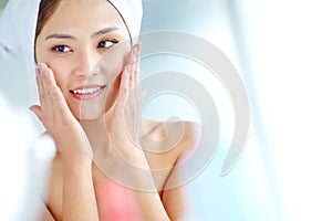 Flawless and radiant skin. An attactive young Asian woman applying moisturizer with a towel on her head.