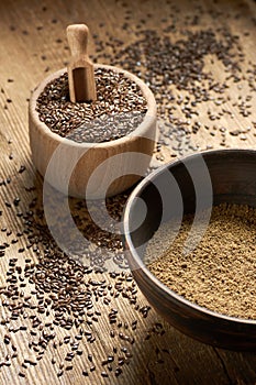 Flax seed coarse ground flour in a clay bowl with linseed wooden bowl nearby on rustic wood