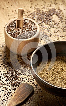 Flax seed coarse ground flour in a clay bowl with linseed wooden bowl nearby on rustic wood