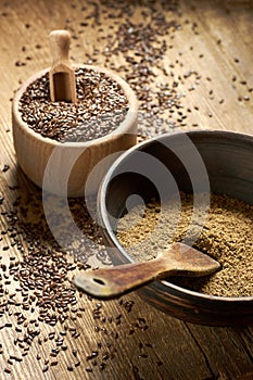 Flax seed coarse ground flour in a clay bowl with linseed wooden bowl nearby on rustic wood