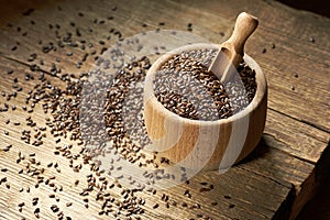 Flax seed in a wooden bowl on rustic wood with grain scattered around