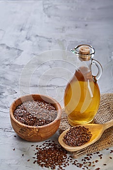 Flax seeds in bowl and flaxseed oil in glass bottle on light textured background, top view, close-up, selective focus