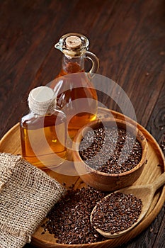 Flax seeds in bowl and flaxseed oil in glass bottle on wooden background, top view, close-up, selective focus