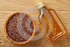 Flax seeds in bowl and flaxseed oil in glass bottle on wooden background, top view, close-up, selective focus