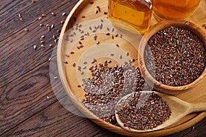 Flax seeds in bowl and flaxseed oil in glass bottle on wooden background, top view, close-up, selective focus