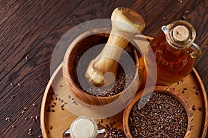 Flax seeds in bowl and flaxseed oil in glass bottle on wooden background, top view, close-up, selective focus