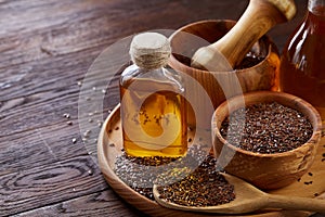 Flax seeds in bowl and flaxseed oil in glass bottle on wooden background, top view, close-up, selective focus.
