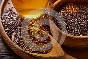 Flax seeds in bowl and flaxseed oil in glass bottle on wooden background, top view, close-up, selective focus