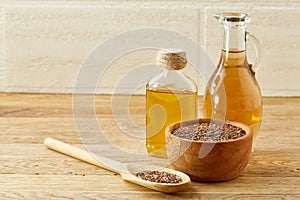 Flax seeds in bowl and flaxseed oil in glass bottle on wooden background, top view, close-up, selective focus