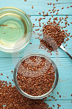 Flax seeds and oil in bowl on blue background. Vertical photo