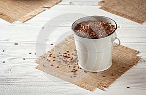 flax seeds in a small enameled bucket on tissue napkin on a white wooden background