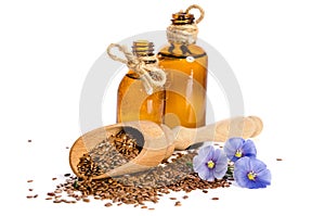 Flax seeds in the wooden scoop, bottle with oil and beauty flowers