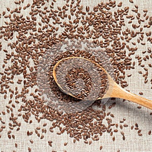 Flax seeds in wooden spoon on fabric background, brown burlap, close-up, top view. Rustic style