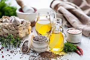 Flaxseed oil in a bottle and ceramic bowl with brown flax seeds and wooden spoon on a white background