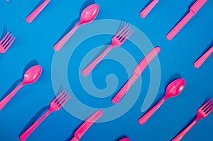 Flay lay photo of pink plastic disposable forks, spoons and knives lying on colorful background. Creative top view