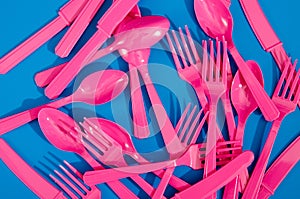 Flay lay photo of pink plastic disposable forks, spoons and knives lying on colorful background. Creative top view