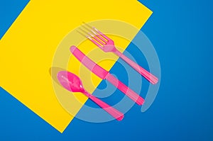 Flay lay photo of pink plastic disposable forks, spoons and knives lying on colorful background. Creative top view