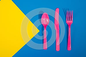 Flay lay photo of pink plastic disposable forks, spoons and knives lying on colorful background. Creative top view