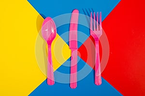 Flay lay photo of pink plastic disposable forks, spoons and knives lying on colorful background. Creative top view