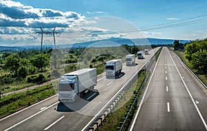 Fleet of light blue transportation trucks in line on a country highway at sunset