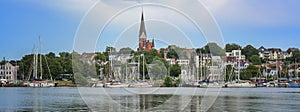 Flensburg panorama, skyline of the city on the east side of the fjord with St. Jurgen church, town houses and sailing ships on the