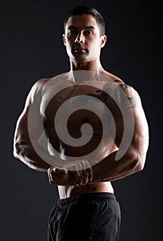Flex now, talk later. athletic young man flexing his muscles while posing against a dark background.