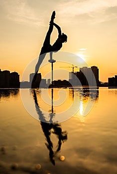 Flexible acrobat doing handstand on the cityscape background during dramatic sunset. Concept of willpower, control and