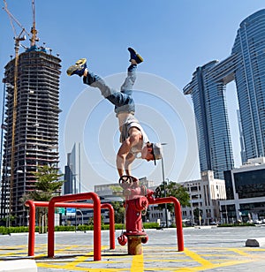 Flexible Acrobat keep balance with one hand on the fireman hydrant with blurred Dubai cityscape. Concept of modern and