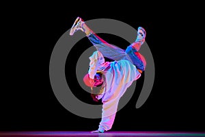 Flexible, artistic young man, breakdancer in motion, performing isolated over black studio background in neon light