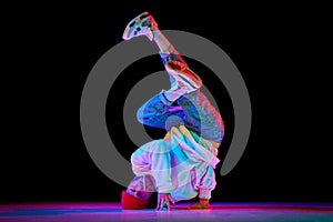 Flexible, artistic young man, breakdancer in motion, performing isolated over black studio background in neon light