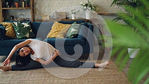 Flexible Asian girl is doing yoga at home sitting on floor and stretching legs and body exercising alone. Beautiful room