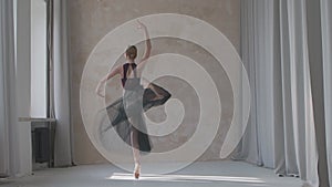 Flexible ballerina in a black transparent skirt performs a pirouette movement by the window. Studio loft style with