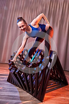 Flexible beautiful gymnast girl doing gymnastic exercises with chair in the hall or on the stage. Young woman jumping in sport