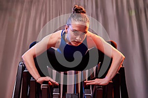 Flexible beautiful gymnast girl doing gymnastic exercises with chair in the hall or on the stage. Young woman jumping in sport