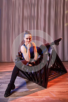 Flexible beautiful gymnast girl doing gymnastic exercises with chair in the hall or on the stage. Young woman jumping in sport