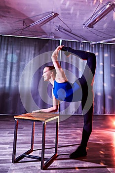 Flexible beautiful gymnast girl doing gymnastic exercises with chair in the hall or on the stage. Young woman jumping in sport